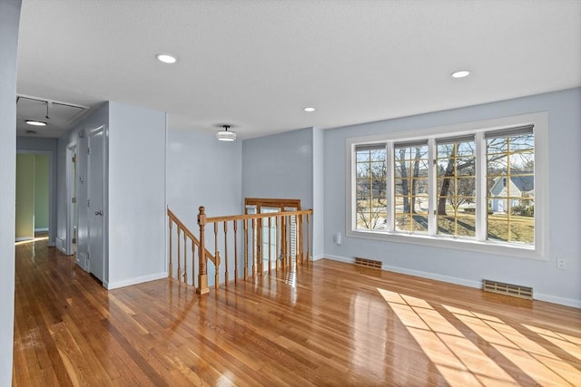 spare room with wood finished floors, visible vents, baseboards, attic access, and recessed lighting