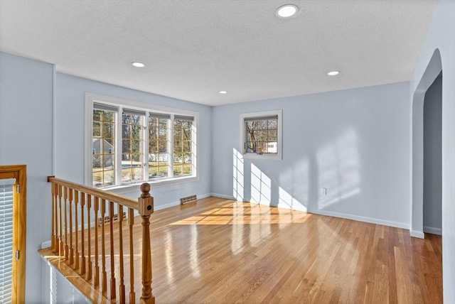 interior space featuring wood finished floors, baseboards, recessed lighting, arched walkways, and a textured ceiling