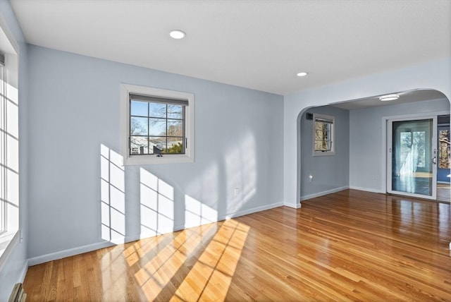 empty room with baseboards, arched walkways, and wood finished floors