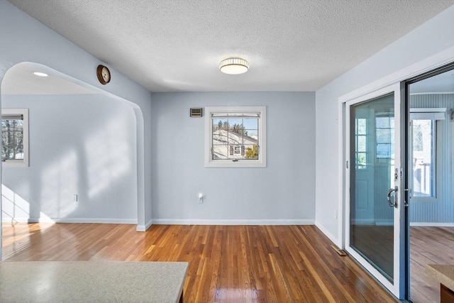 empty room featuring a textured ceiling, wood finished floors, arched walkways, and baseboards