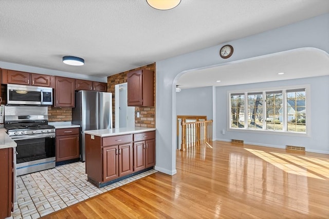 kitchen with tasteful backsplash, arched walkways, stainless steel appliances, and light countertops