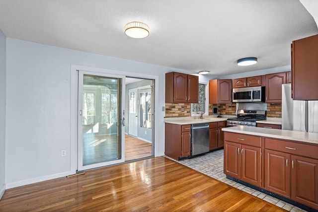 kitchen with a sink, backsplash, stainless steel appliances, light wood finished floors, and light countertops