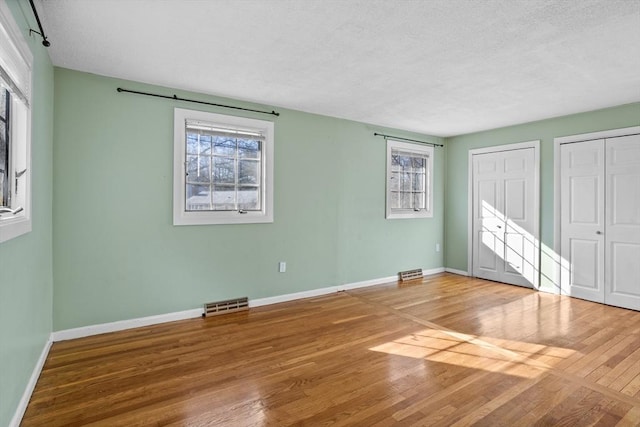 unfurnished bedroom with visible vents, multiple closets, baseboards, and wood finished floors