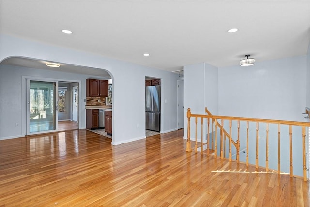 empty room featuring recessed lighting, arched walkways, light wood finished floors, and baseboards