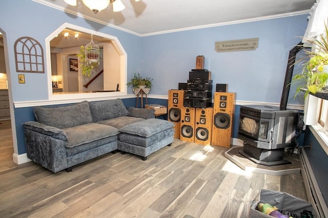 living room featuring wood finished floors, crown molding, a wood stove, arched walkways, and baseboard heating