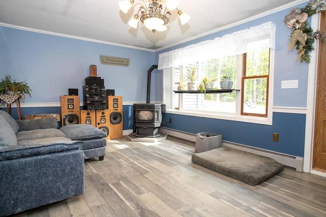 living area with a wood stove, a baseboard heating unit, ornamental molding, wood finished floors, and baseboards
