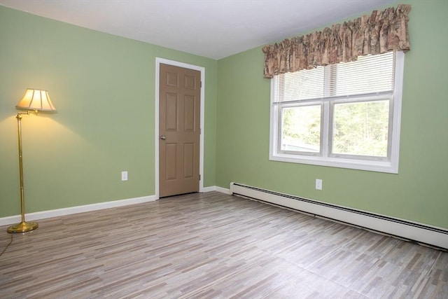empty room featuring a baseboard heating unit, wood finished floors, and baseboards