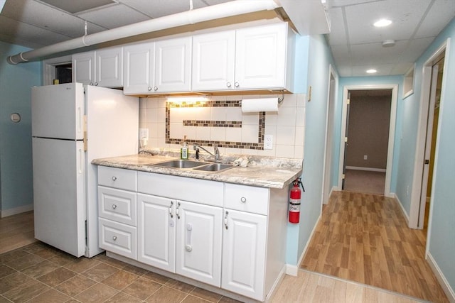 kitchen featuring freestanding refrigerator, a sink, baseboards, white cabinets, and recessed lighting
