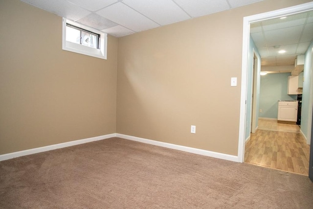 unfurnished room with a paneled ceiling, light colored carpet, and baseboards
