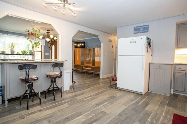 kitchen with freestanding refrigerator, gray cabinetry, a chandelier, crown molding, and arched walkways