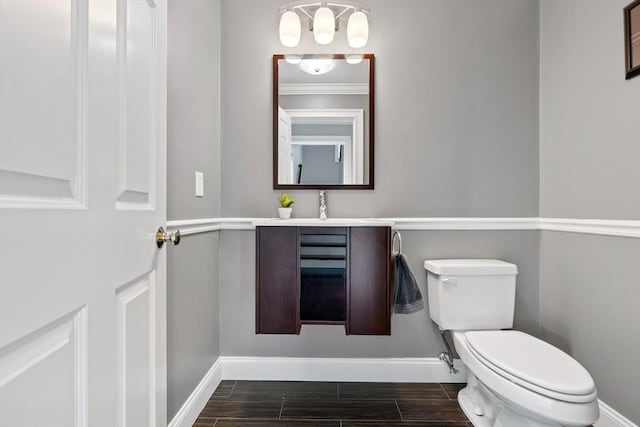 bathroom with baseboards, wood finished floors, toilet, and vanity