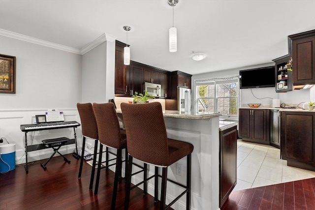 kitchen with a kitchen bar, crown molding, hanging light fixtures, dark brown cabinets, and stainless steel fridge with ice dispenser