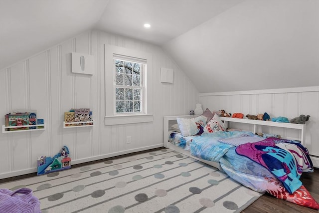 bedroom with wood finished floors, lofted ceiling, and a decorative wall