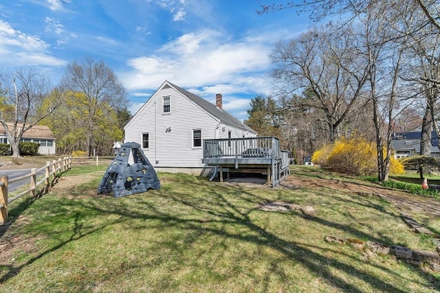 back of house featuring fence, a wooden deck, a chimney, and a yard