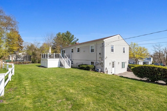 back of house featuring a lawn, a trampoline, stairs, and a wooden deck
