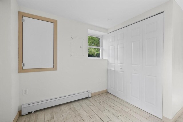 unfurnished bedroom featuring baseboards, a baseboard heating unit, and light wood finished floors