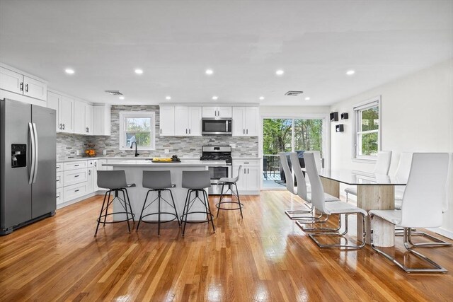 kitchen with a breakfast bar area, stainless steel appliances, white cabinets, and decorative backsplash