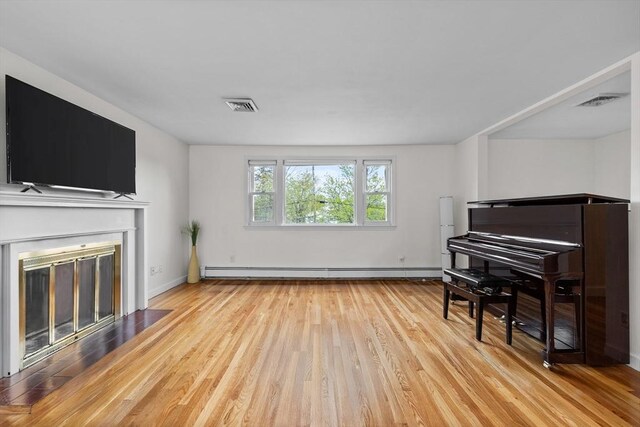 living area with visible vents, a fireplace with flush hearth, wood finished floors, and baseboard heating