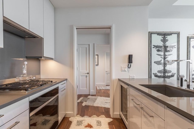 kitchen featuring dark hardwood / wood-style flooring, stainless steel gas cooktop, sink, white cabinetry, and oven