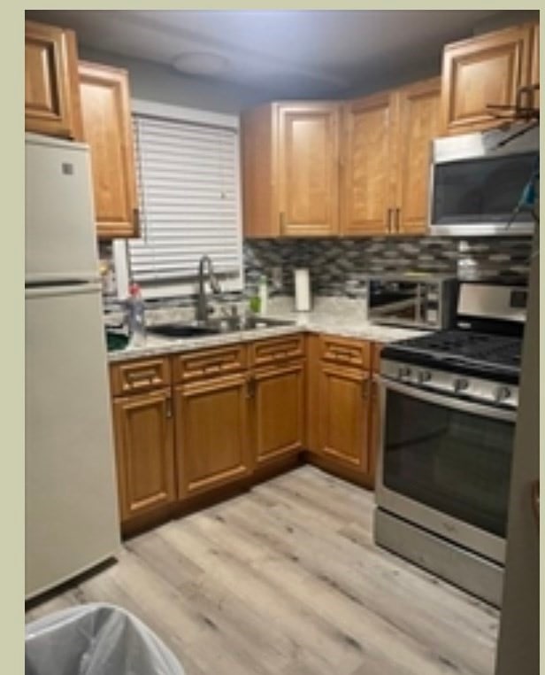 kitchen with decorative backsplash, light wood-type flooring, stainless steel appliances, and sink