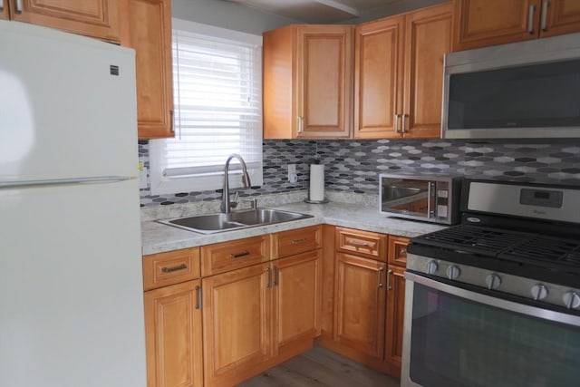 kitchen featuring backsplash, sink, light hardwood / wood-style flooring, light stone countertops, and appliances with stainless steel finishes