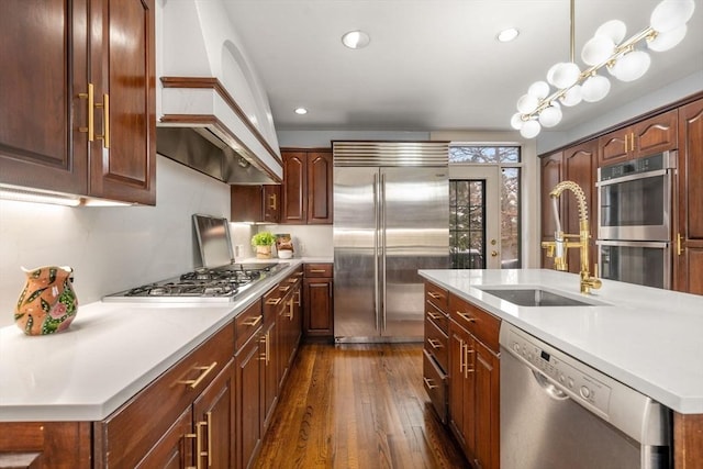 kitchen featuring a center island with sink, appliances with stainless steel finishes, sink, pendant lighting, and dark wood-type flooring