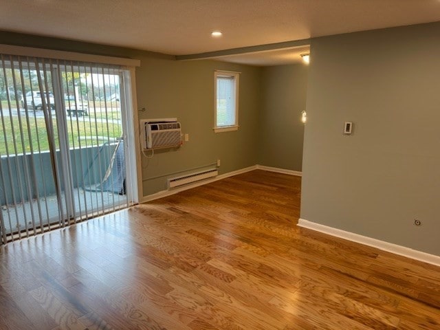 empty room featuring wood-type flooring, a wall unit AC, and baseboard heating