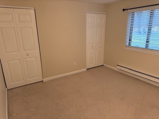 unfurnished bedroom with baseboard heating, multiple closets, and light colored carpet