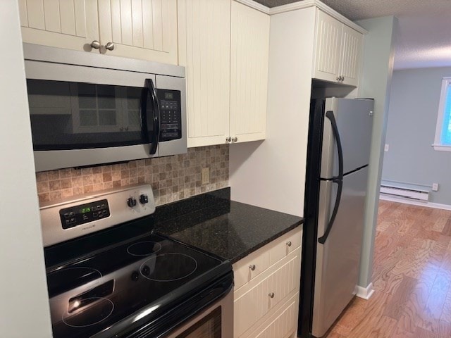 kitchen featuring appliances with stainless steel finishes, light wood-type flooring, tasteful backsplash, a baseboard heating unit, and dark stone countertops