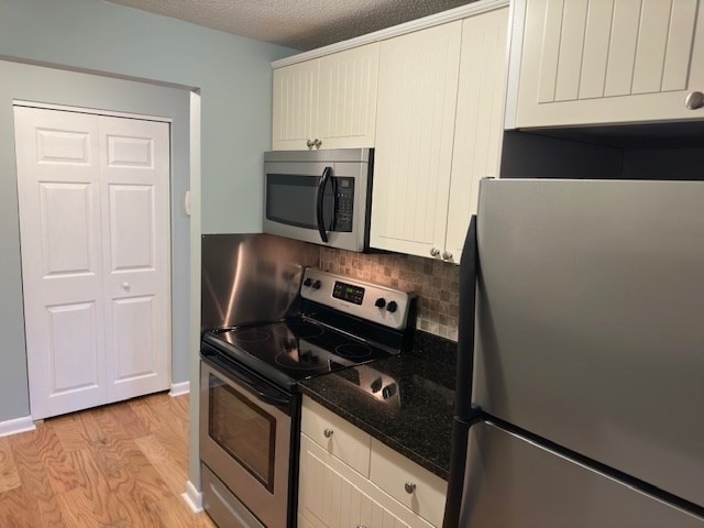 kitchen featuring stainless steel appliances, light hardwood / wood-style flooring, dark stone countertops, cream cabinets, and a textured ceiling