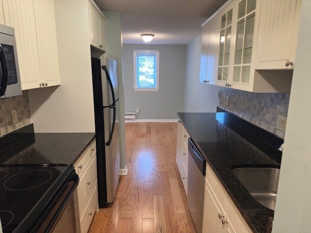 kitchen featuring stainless steel appliances, dark stone counters, decorative backsplash, white cabinets, and light wood-type flooring