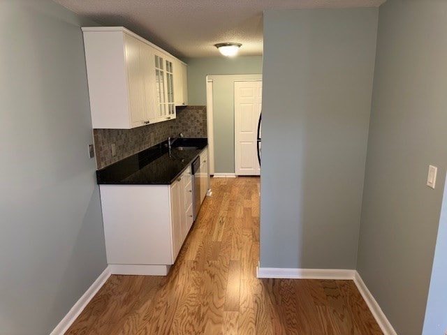 kitchen with tasteful backsplash, sink, dishwasher, white cabinets, and light hardwood / wood-style floors