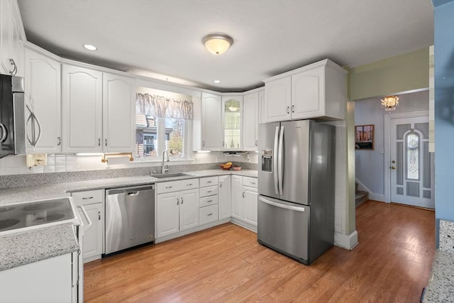 kitchen featuring white cabinetry, a sink, light wood finished floors, backsplash, and stainless steel appliances