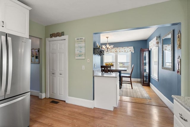kitchen with freestanding refrigerator, baseboards, white cabinets, light wood-style flooring, and a notable chandelier