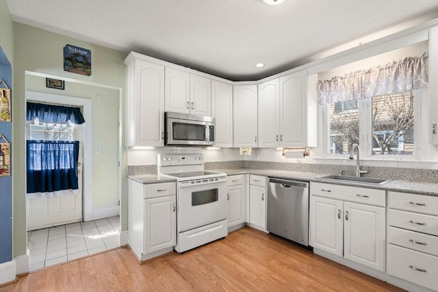 kitchen featuring appliances with stainless steel finishes, a sink, light wood-style floors, light countertops, and white cabinetry