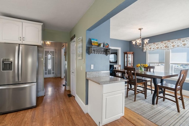 kitchen with stainless steel refrigerator with ice dispenser, pendant lighting, light wood finished floors, a notable chandelier, and white cabinetry