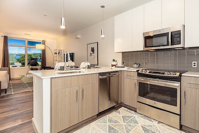 kitchen with pendant lighting, light hardwood / wood-style floors, stainless steel appliances, sink, and kitchen peninsula