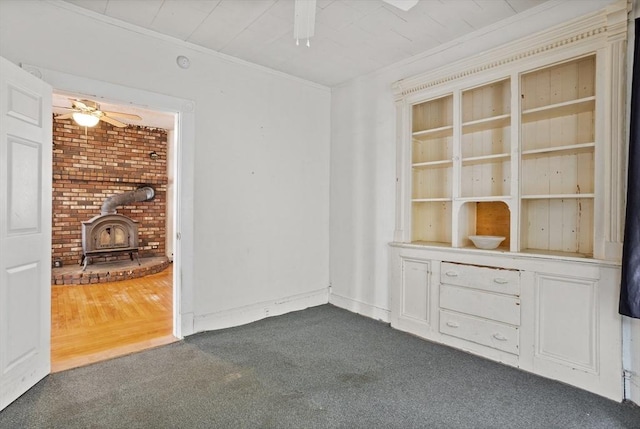 spare room with dark colored carpet, a wood stove, a ceiling fan, and crown molding