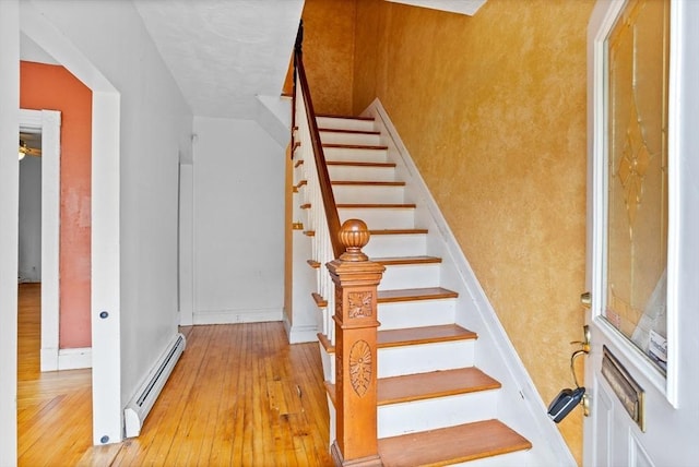 staircase featuring baseboard heating, hardwood / wood-style flooring, and baseboards