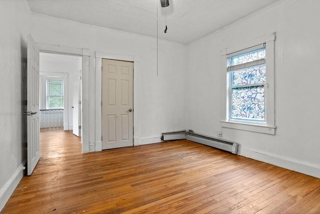 empty room featuring healthy amount of natural light, light wood-style flooring, a baseboard heating unit, crown molding, and baseboards