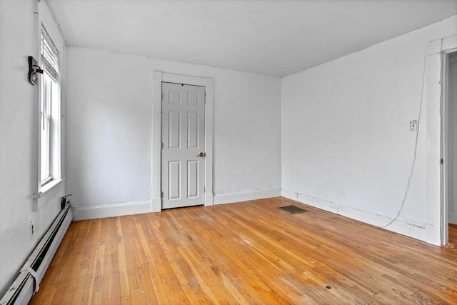 empty room with a baseboard radiator, light wood finished floors, and baseboards