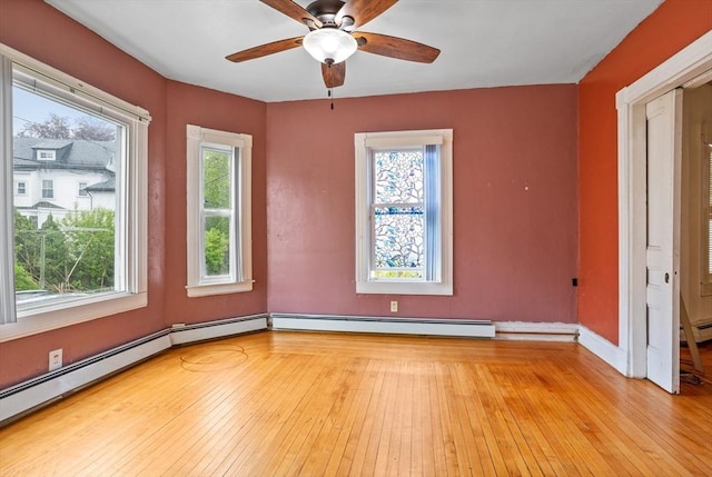 empty room featuring plenty of natural light, a baseboard heating unit, ceiling fan, and light wood-style flooring