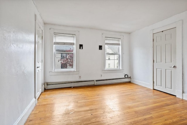 unfurnished room with a baseboard radiator, light wood-style floors, and baseboards