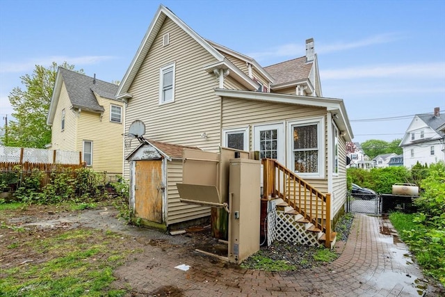 back of property featuring fence, a storage unit, a chimney, an outdoor structure, and a shingled roof