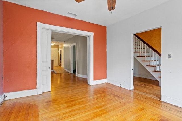 empty room featuring ceiling fan, light wood finished floors, stairway, and baseboards