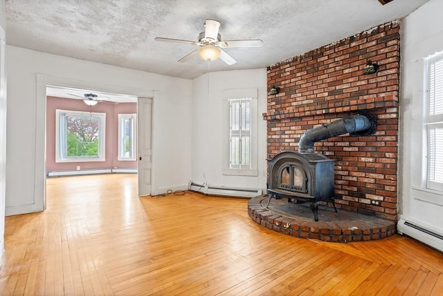 unfurnished living room featuring a baseboard radiator, a wood stove, plenty of natural light, ceiling fan, and a textured ceiling