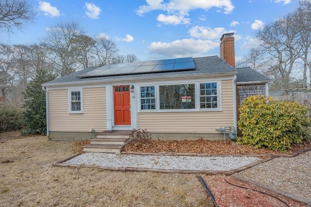 bungalow-style house with solar panels, a chimney, and a shingled roof