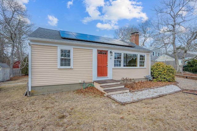 bungalow-style house with solar panels, fence, roof with shingles, and a chimney