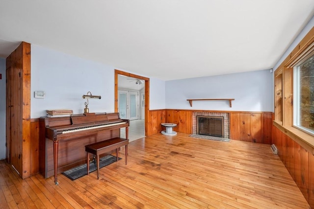 living area with wainscoting, a brick fireplace, wood walls, and wood-type flooring