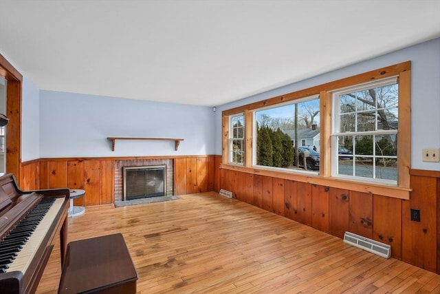 living area with visible vents, a brick fireplace, hardwood / wood-style floors, and a wainscoted wall